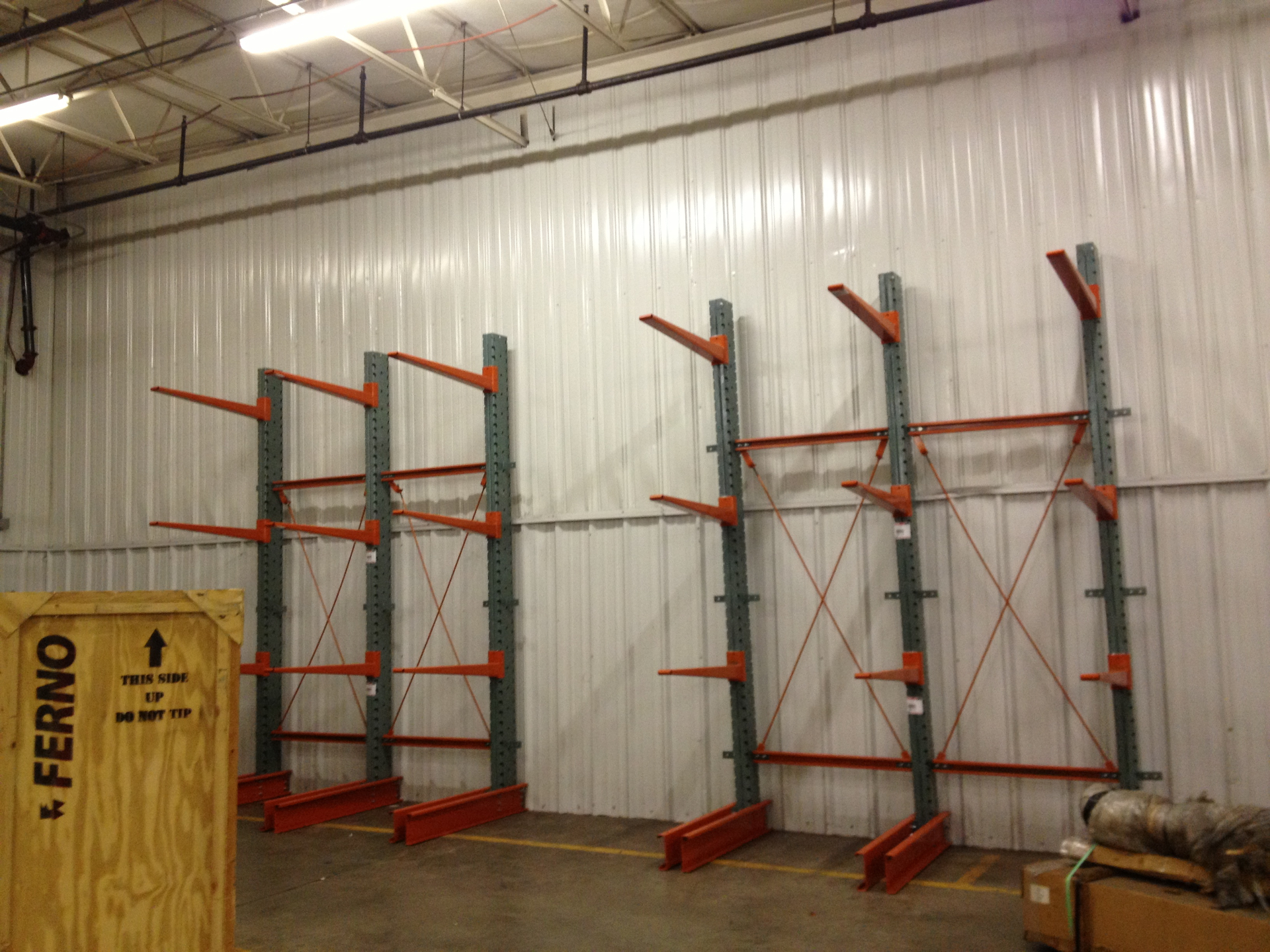 Cantilever racking with orange arms and green columns installed against warehouse wall for long-load storage