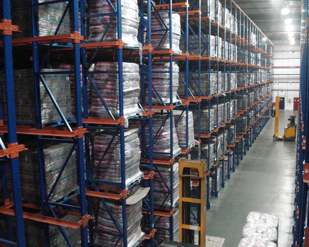Tall drive-in pallet racking with blue uprights and orange rails storing palletized beverage product